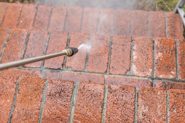 Stock image of a middle aged man powerwashing a home.