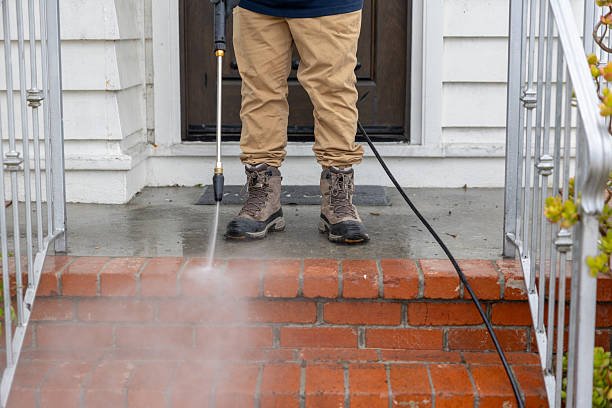 Stock image of a middle aged man powerwashing a home.